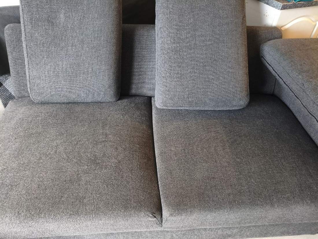 Graues Sofa mit Ottomane und sichtbaren Verschmutzungen vor der Reinigung
